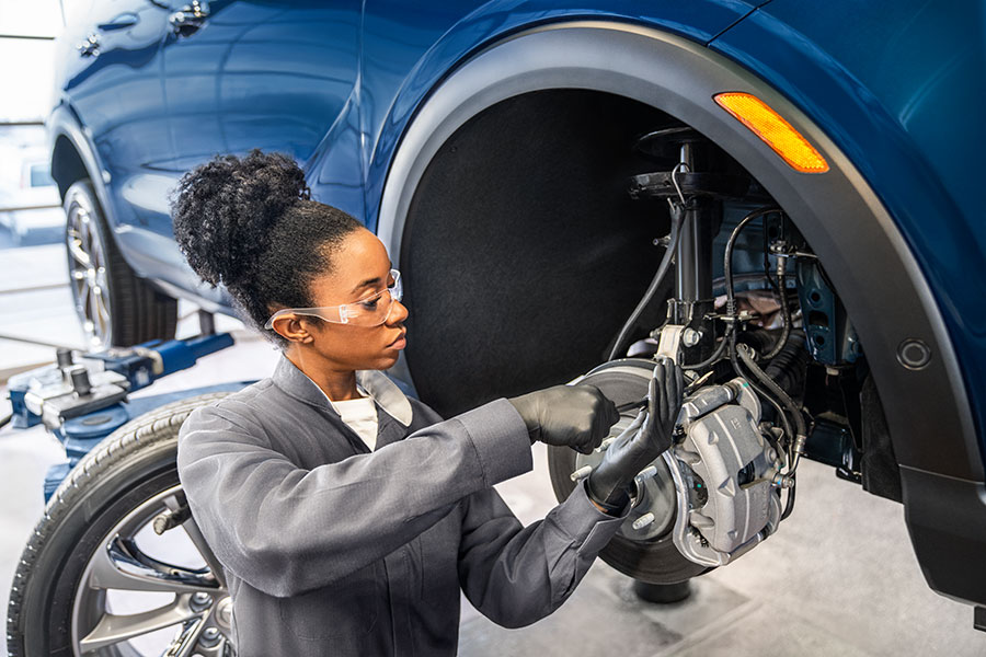 Female mechanic working on a vehicle's front brake and suspension assembly.