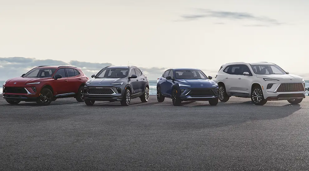 Four Buick SUVs lined up on a coastal road next to the ocean.