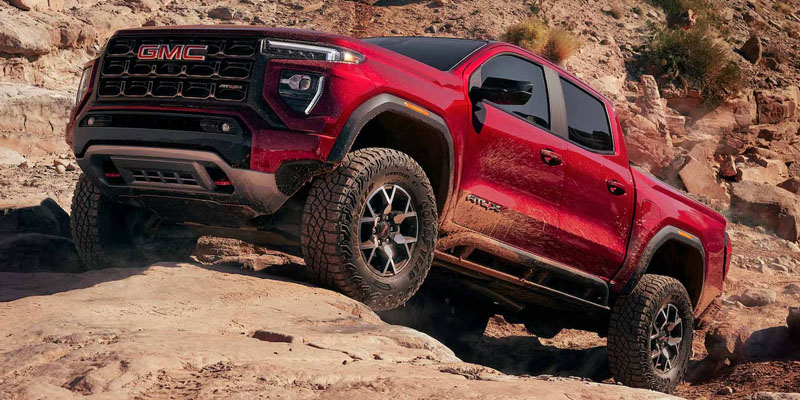 Red GMC Canyon AT4X pickup truck driving over rocky terrain.