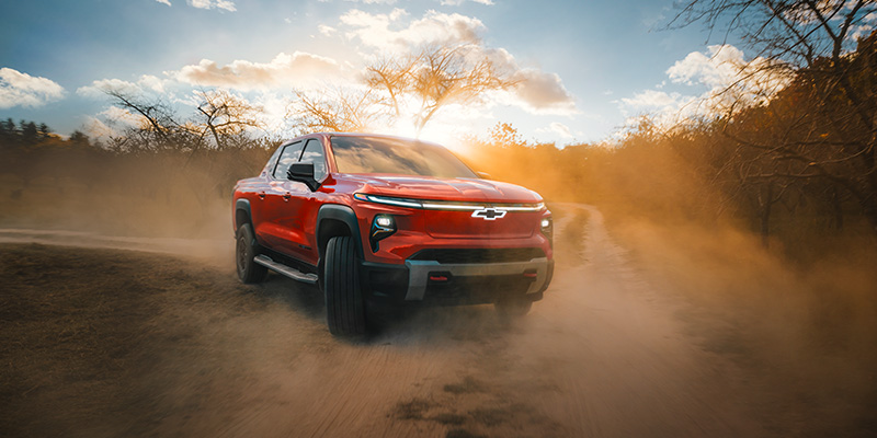 Red Chevrolet Silverado EV pickup truck kicking up dust on a dirt trail.